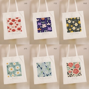 May include: Six white tote bags with floral patterns and the month and flower name printed on each bag. The flowers are carnation, violet, daffodil, daisy, lily of the valley, and rose.