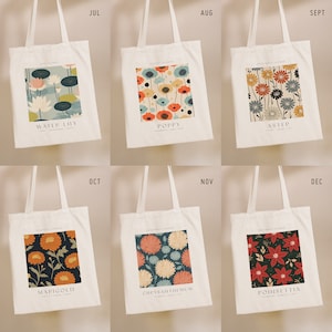 May include: Six white tote bags with different floral designs and month names printed on them. The designs include water lily, poppy, aster, marigold, chrysanthemum, and poinsettia.