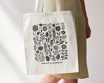 May include: A white canvas tote bag with black floral print and the text "A Vibrant & Flourishing".