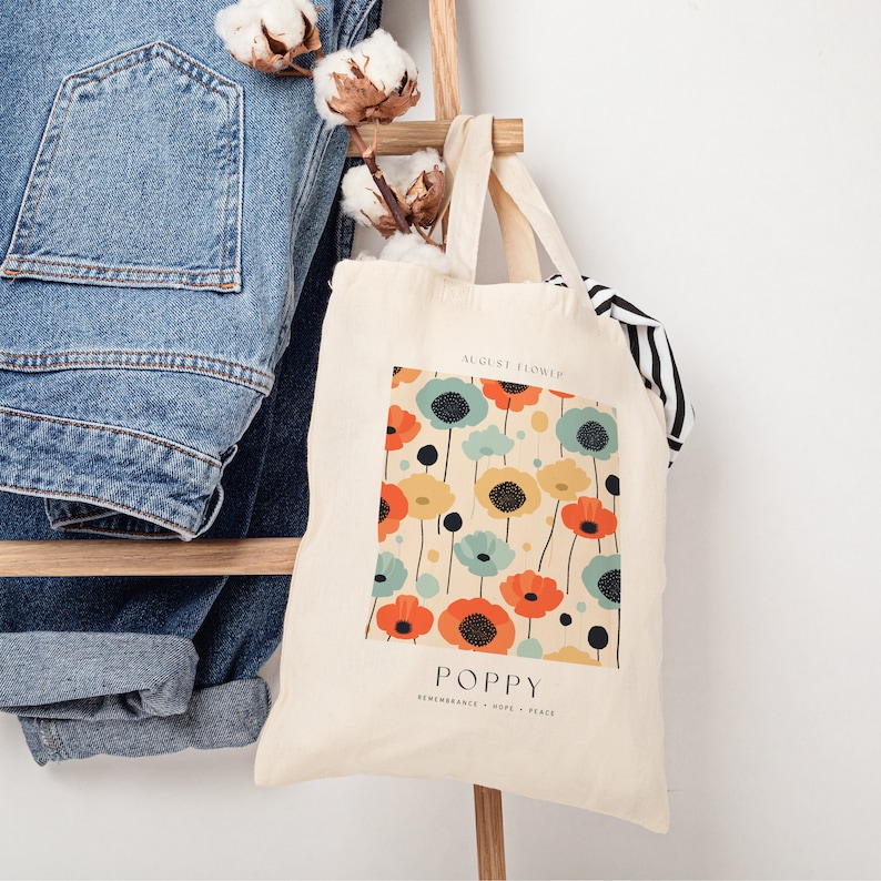 May include: A white canvas tote bag with a colorful poppy flower pattern. The bag has the text "August Flower" and "Poppy" printed on it. The text "Remembrance - Hope - Peace" is also printed on the bag.