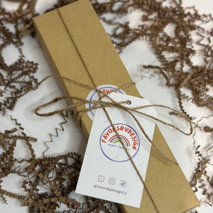 May include: A brown cardboard box tied with twine and a white tag. The tag has a logo that says "Favors By Design Party Favors" with a rainbow and the text "@FavorsByDesignCo".