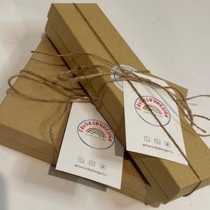 May include: Three brown cardboard boxes with twine tied around them. The boxes are stacked on top of each other. Each box has a white sticker with a rainbow logo and the text "FavorsByDesign Party Favors" and the text "@FavorsByDesignCo".