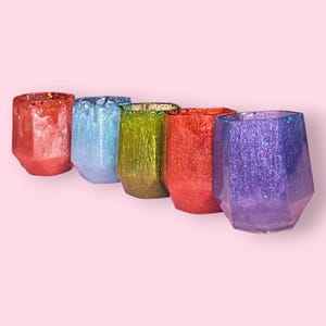 Peut inclure: Cinq bougeoirs en verre de forme géométrique dans un arc-en-ciel de couleurs. Les bougeoirs sont rouge, bleu, vert, orange et violet. Chaque bougeoir a une finition scintillante.