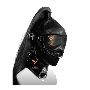 Op de afbeelding: Zwarte leren kap met een blinddoek, neusring en halsband. De kap heeft een hoge paardenstaart en is vastgezet met gespen. Het woord "Attire" is in koperkleur op de kap en kraag gedrukt.