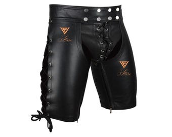 May include: Black leather chaps with a lace-up front and side detailing. The chaps have a zipper closure on the side and feature the word "Attire" in a copper-colored font. The waist has silver button accents.