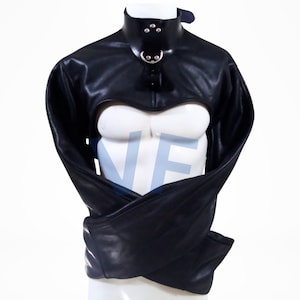 Puede incluir: Prenda de restricción de cuero negro con mangas largas y cuello. La prenda tiene un anillo de metal en el cuello y una correa que va alrededor del cuello.