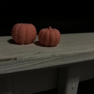 Puede incluir: Dos peque&ntilde;as velas rosadas en forma de calabaza sobre una superficie de madera blanca.