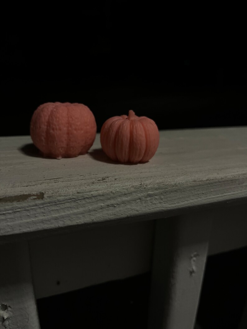 Puede incluir: Dos peque&ntilde;as velas rosadas en forma de calabaza sobre una superficie de madera blanca.