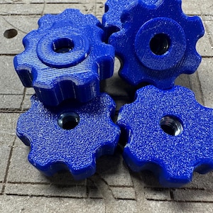 May include: A close-up shot of five bright blue, gear-shaped knobs. Each knob has a central hole with a metal insert. The knobs are arranged on a textured, brown surface.