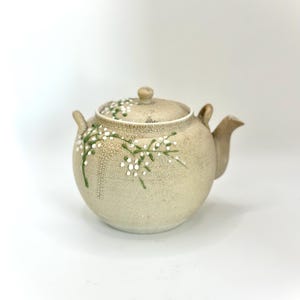 May include: A white ceramic mug with a black handle and the text "But First, Coffee" in a handwritten style. The mug is on a white surface. The mug is approximately 4 inches tall.