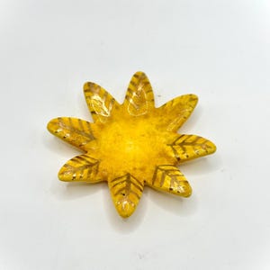 Op de afbeelding: Een gele, stervormige keramische schaal met acht punten. Elke punt heeft een bladgoud ontwerp. De schaal staat op een witte achtergrond. De schaal is waarschijnlijk handgemaakt en kan als decoratieartikel worden gebruikt.
