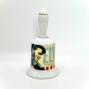 Puede incluir: Campana de cerámica blanca con ribete dorado. La campana presenta una imagen colorida de Elvis Presley con el texto "Elvis The King" en la parte delantera.