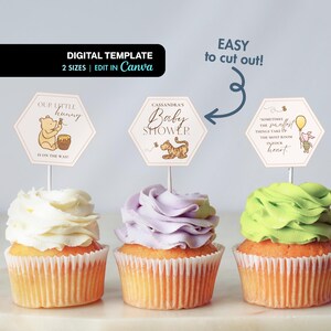 May include: Three cupcakes with different colored frosting, each topped with a Winnie the Pooh-themed decoration. The decorations are hexagonal and feature illustrations and text for a baby shower. The text includes "Our Little Hunny", "Cassandra's Baby Shower", and a quote.