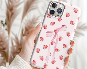 May include: A white phone case with a pattern of pink strawberries and a pink bow. The case has a glossy finish and is designed to fit a smartphone. The strawberries are scattered across the surface.