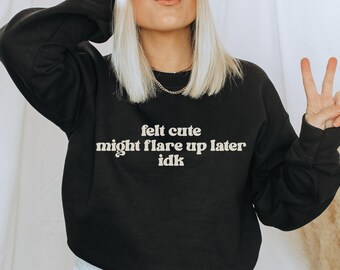 May include: Black sweatshirt with the text "felt cute might flare up later idk" in a white, sans-serif font. The sweatshirt is a crew neck style. The image shows a person wearing the sweatshirt.