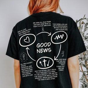 May include: Black t-shirt with a white graphic design of a circle with the words "Good News" inside. The graphic also includes arrows and text about God's love and sacrifice.