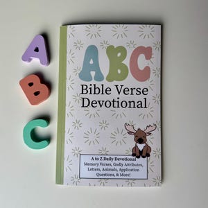 May include: A colorful book titled "ABC Bible Verse Devotional" with a cartoon moose on the cover. The book features a daily devotional with memory verses, godly attributes, letters, animals, application questions, and more.