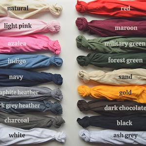 May include: A collection of folded t-shirts in various colors, including natural, light pink, azalea, indigo, navy, graphite heather, dark grey heather, charcoal, white, red, maroon, military green, forest green, sand, gold, dark chocolate, black, and ash grey.