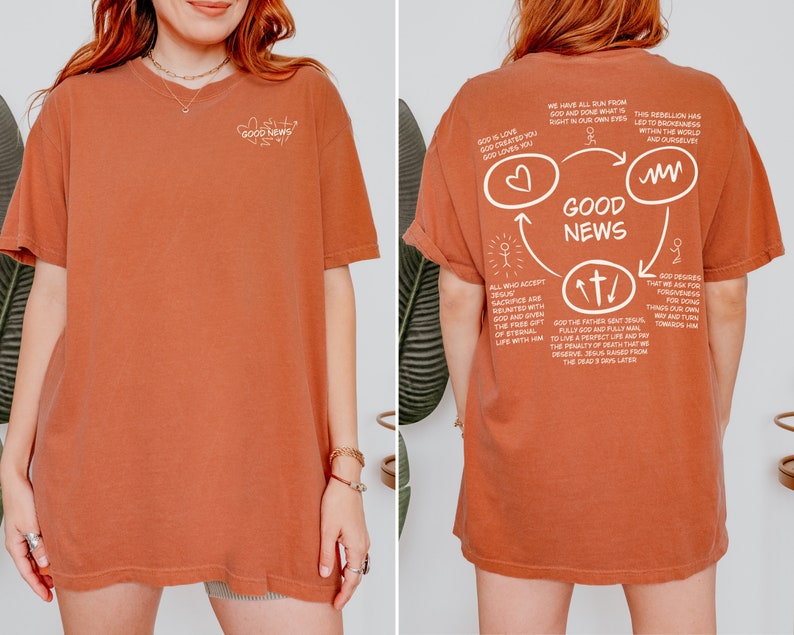 May include: A rust-colored t-shirt with a white graphic design on the back. The graphic features a circle with the words "Good News" inside. The circle is surrounded by arrows and other symbols, and includes text about God's love and sacrifice.