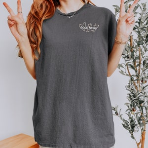 May include: A charcoal gray oversized t-shirt with a graphic of hearts and the text "GOOD NEWS" in white.