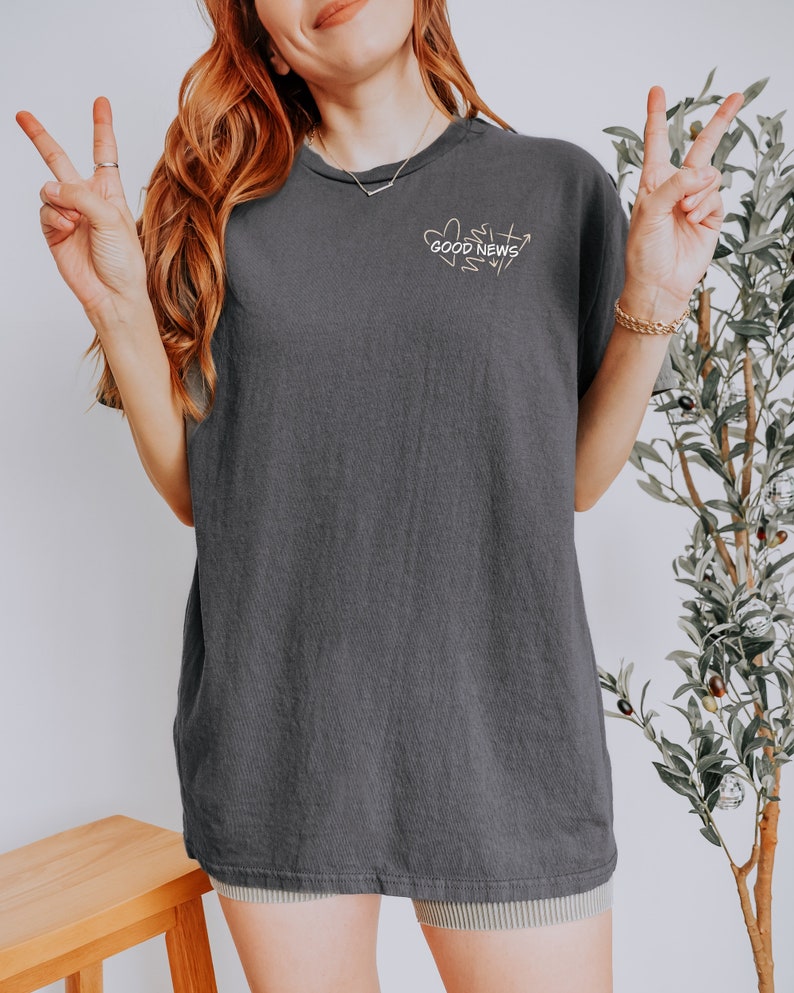 May include: A charcoal gray oversized t-shirt with a graphic of hearts and the text "GOOD NEWS" in white.