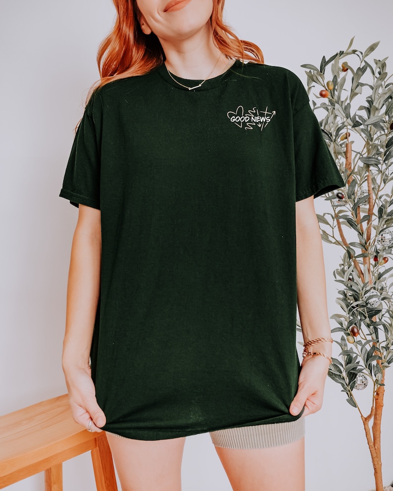 May include: A black t-shirt with a white graphic design that says "GOOD NEWS" with a heart and arrow design.
