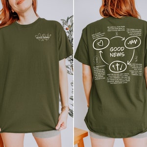 May include: A green t-shirt with a white graphic on the back. The graphic is a circle with arrows pointing in different directions. The text in the graphic says "GOOD NEWS" and includes a heart, a cross, and a wavy line. The text on the front of the shirt says "GOOD NEWS".