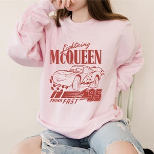 a woman sitting on a chair wearing a pink sweatshirt