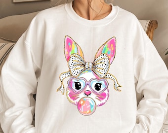 May include: White sweatshirt with a colorful cartoon bunny wearing heart-shaped glasses and a bow. The bunny is holding a pink and blue bubble.