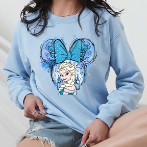 a woman wearing a blue sweatshirt with a cartoon character on it