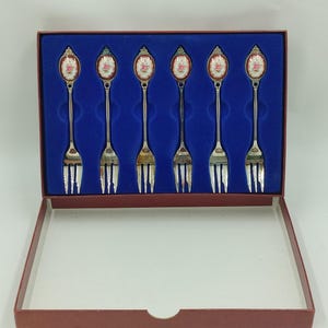 May include: Set of six silver-plated forks with floral designs on the handles, displayed in a red velvet box with a blue velvet interior.