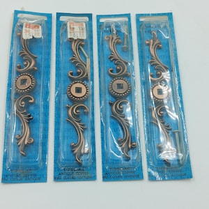 May include: Four packs of antique copper drawer pulls with ornate designs. Each pack includes a pull and a screw. The packs are labelled "Antique Copper" and "Fini Cuivre Antique".