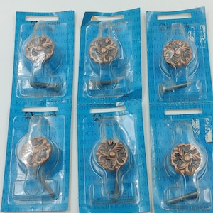 May include: Six packs of antique copper cabinet knobs with a floral design. Each pack includes a knob and a screw.