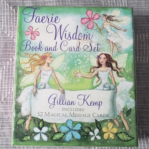 Peut inclure: Un coffret intitulé "Faerie Wisdom Book and Card Set" par Gillian Kemp. La couverture présente des illustrations de fées, de fleurs et le texte "Includes 52 Magical Message Cards". La palette de couleurs est principalement verte, bleue et rose.