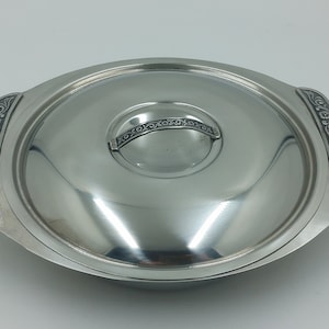 Peut inclure: Un plat de service en argent avec un couvercle. Le couvercle a une poignée décorative et un motif floral autour du bord.