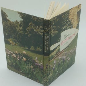 May include: An open book titled "The Canadian Gardener's Guide." The cover features a landscape scene with a garden, trees, and a building. The spine reads "The Canadian Gardeners Guide."
