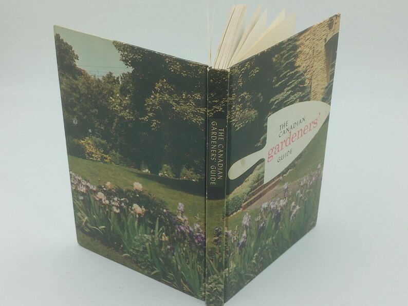May include: An open book titled "The Canadian Gardener's Guide." The cover features a landscape scene with a garden, trees, and a building. The spine reads "The Canadian Gardeners Guide."