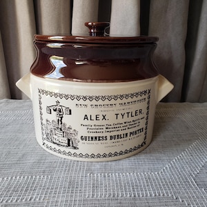Op de afbeelding: Een vintage bruin en crème stenen pot met een deksel. De pot heeft een gedetailleerd zwart-wit etiket met de tekst "ALEX. TYTLER" en "GUINNESS DUBLIN PORTER". Het heeft twee handvatten aan de zijkant en een kleine knop op het deksel.