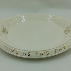 May include: White oval serving platter with gold trim and the words "Give Us This Day" written around the edge.