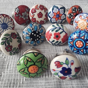 Peut inclure: Ensemble de boutons de meubles en céramique avec divers motifs floraux. Les boutons présentent un mélange de couleurs, dont le rouge, le bleu, l'orange et le vert, sur fond blanc. Chaque bouton a une base en métal argenté.