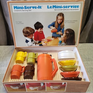 May include: A retro children's serving set in its original box. The set includes an orange jug, mugs in yellow, green, orange, and brown, and bowls in yellow, green, orange, and brown. The box features the text "Mini-Serve-It" and "Le Mini-service".
