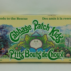 May include: A yellow and green board game box with the title "Cabbage Patch Kids" and the text "Friends to the Rescue" and "Des amis à la rescousse". The box features a cartoon image of a Cabbage Patch Kid.