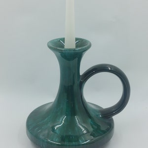 May include: A teal green ceramic candle holder with a black handle. The holder has a wide base and a narrow neck with a single candle holder on top.