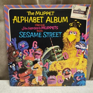 May include: Vintage vinyl record album cover for "The Muppet Alphabet Album" starring Jim Henson's Muppets from Sesame Street. The cover features a black background with colourful Muppet characters and the alphabet. Big Bird is prominently displayed.