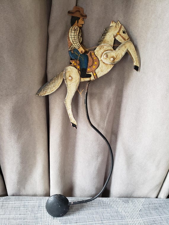 A hand-carved wooden cowboy and horse that balances and rocks kinetically — vintage folk art with the charm of something found at a dusty estate sale.