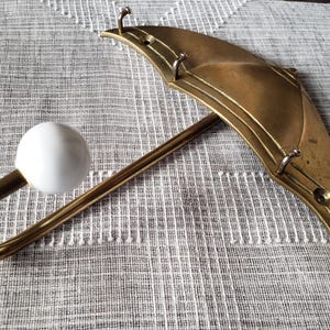 May include: A brass-coloured umbrella-shaped wall hook with a white spherical knob. The hook has a curved handle and a decorative umbrella top with three small hooks. The item is designed for hanging items.