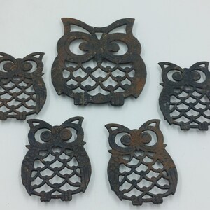 May include: Five cast iron owl-shaped hot pads. The owls are all the same design, with a detailed cut-out pattern and a rustic brown finish.