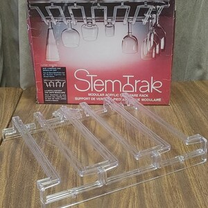 May include: Clear acrylic StemTrak modular glassware rack with a box featuring a display of hanging wine glasses. The box reads "StemTrak" and "Modular Acrylic Stemware Rack". Several clear acrylic rack components are visible.