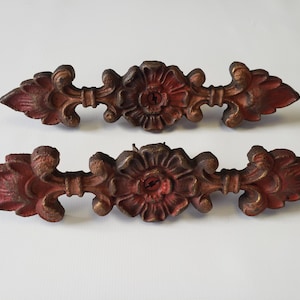 May include: Two antique, ornate metal drawer pulls. Each pull is a reddish-brown colour with a floral centre and decorative end pieces. The pulls are approximately 20 cm long.