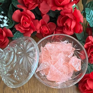 May include: A clear glass bowl filled with pink rock candy, surrounded by red silk roses.